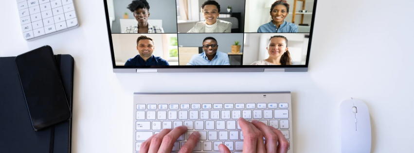 Person typing on white keyboard with computer screen showing six diverse people in a video conference call