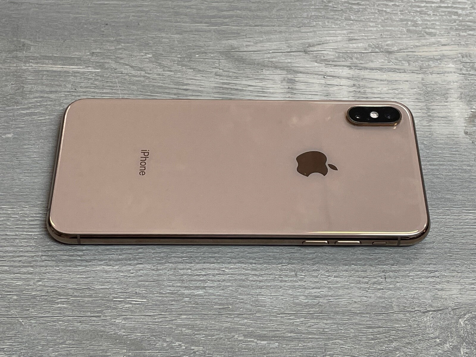 Apple iPhone XS Max in gold color lying face down showing dual camera and sleek design on wooden surface