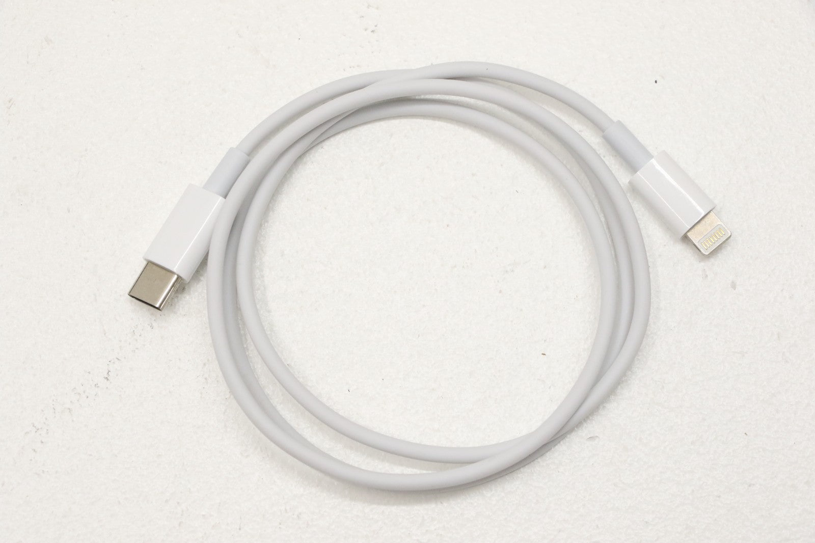 White Apple USB-C to Lightning charging cable coiled on white surface for wireless headset accessories