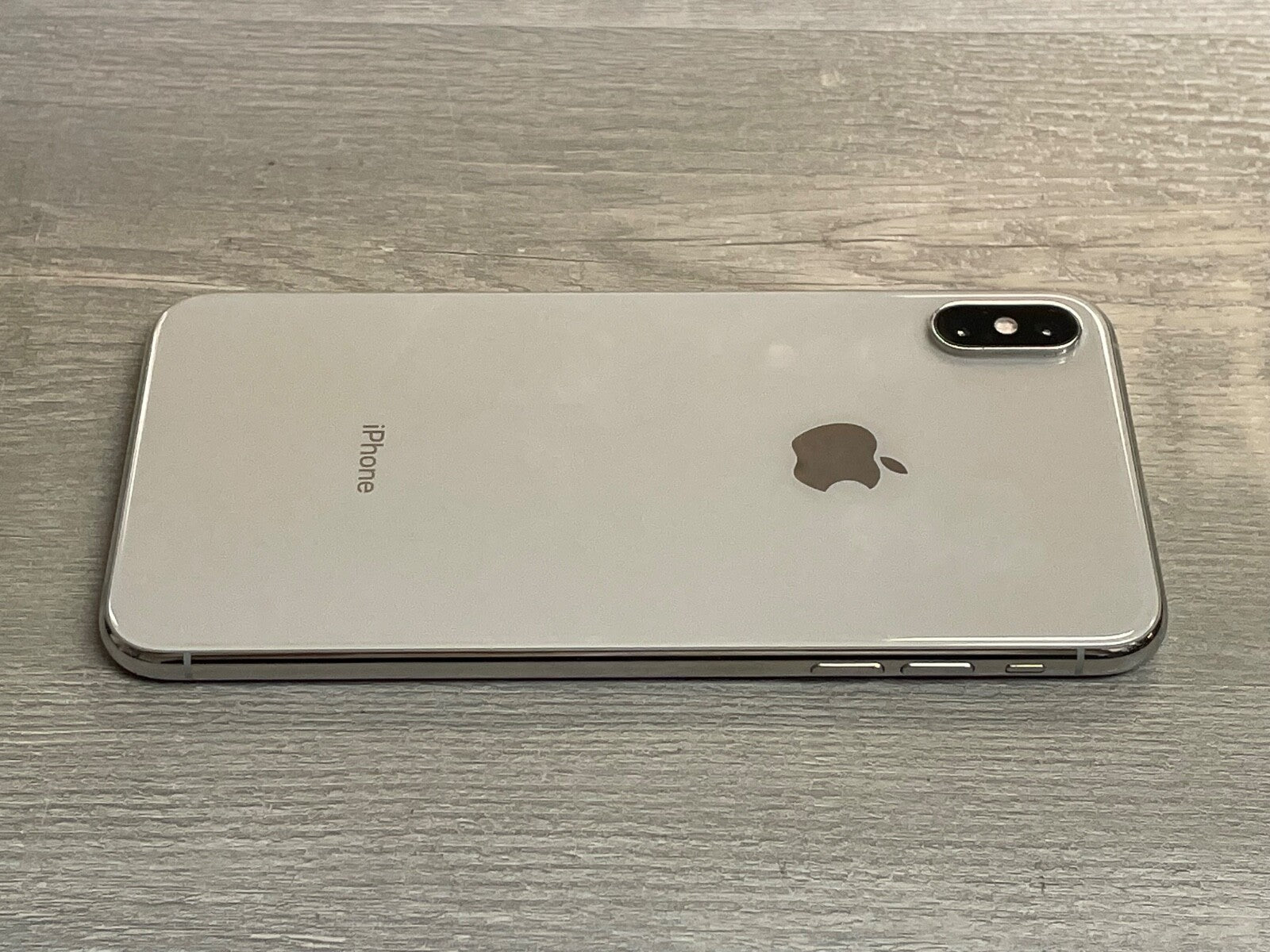 Silver Apple iPhone XS Max lying face down on wooden surface showing dual camera and side buttons