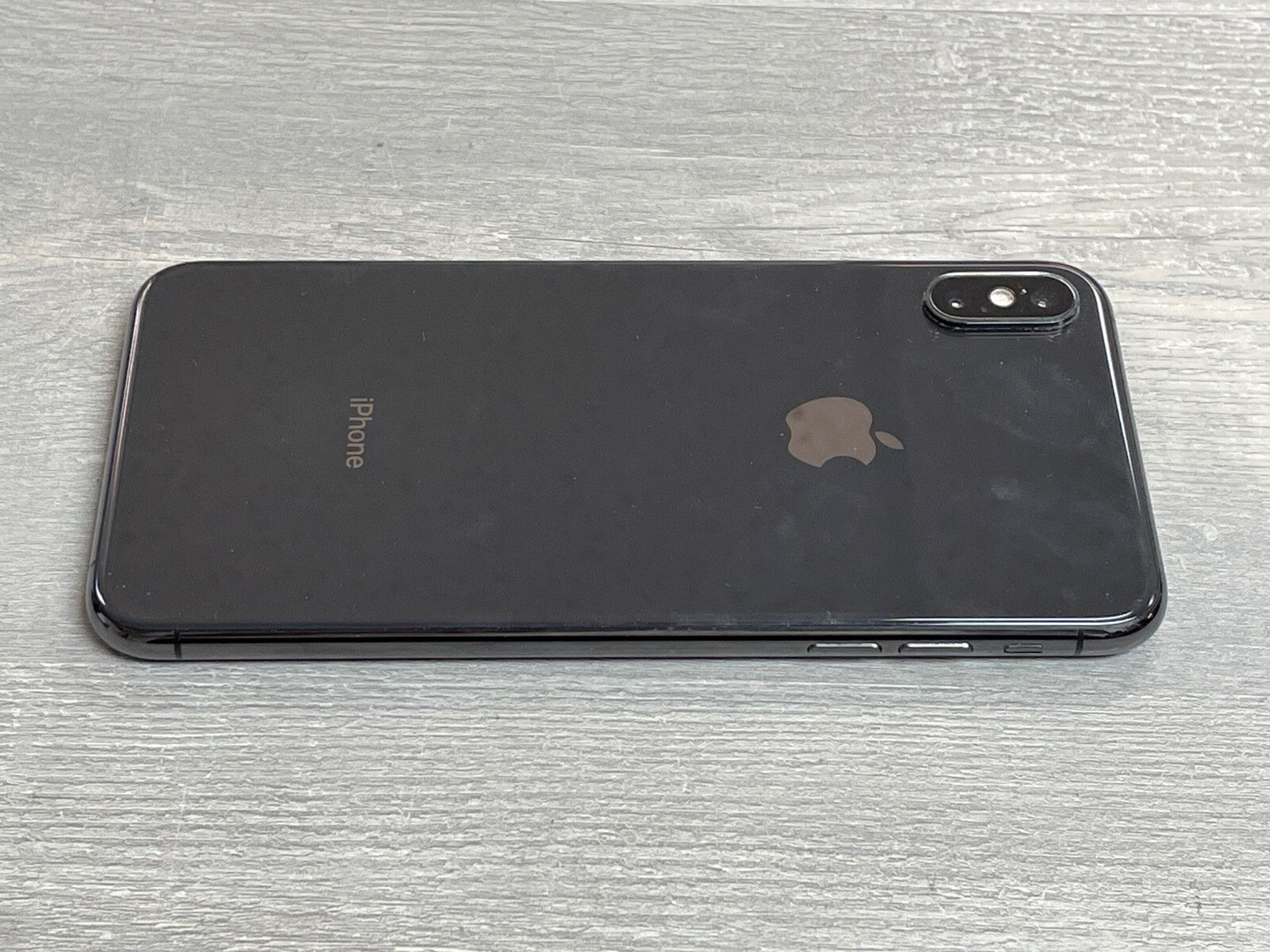 Black Apple iPhone XS Max with dual camera lying face down on a gray wooden surface showing its sleek design