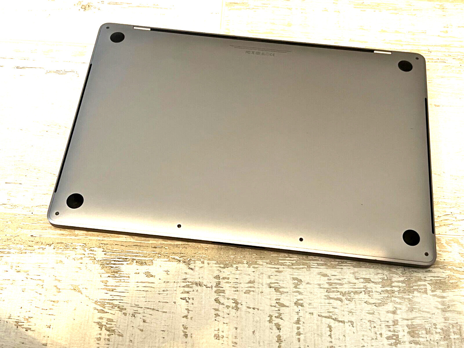 Apple MacBook Pro 15-inch bottom view showing Sequoia color aluminum case with rubber feet and screws visible