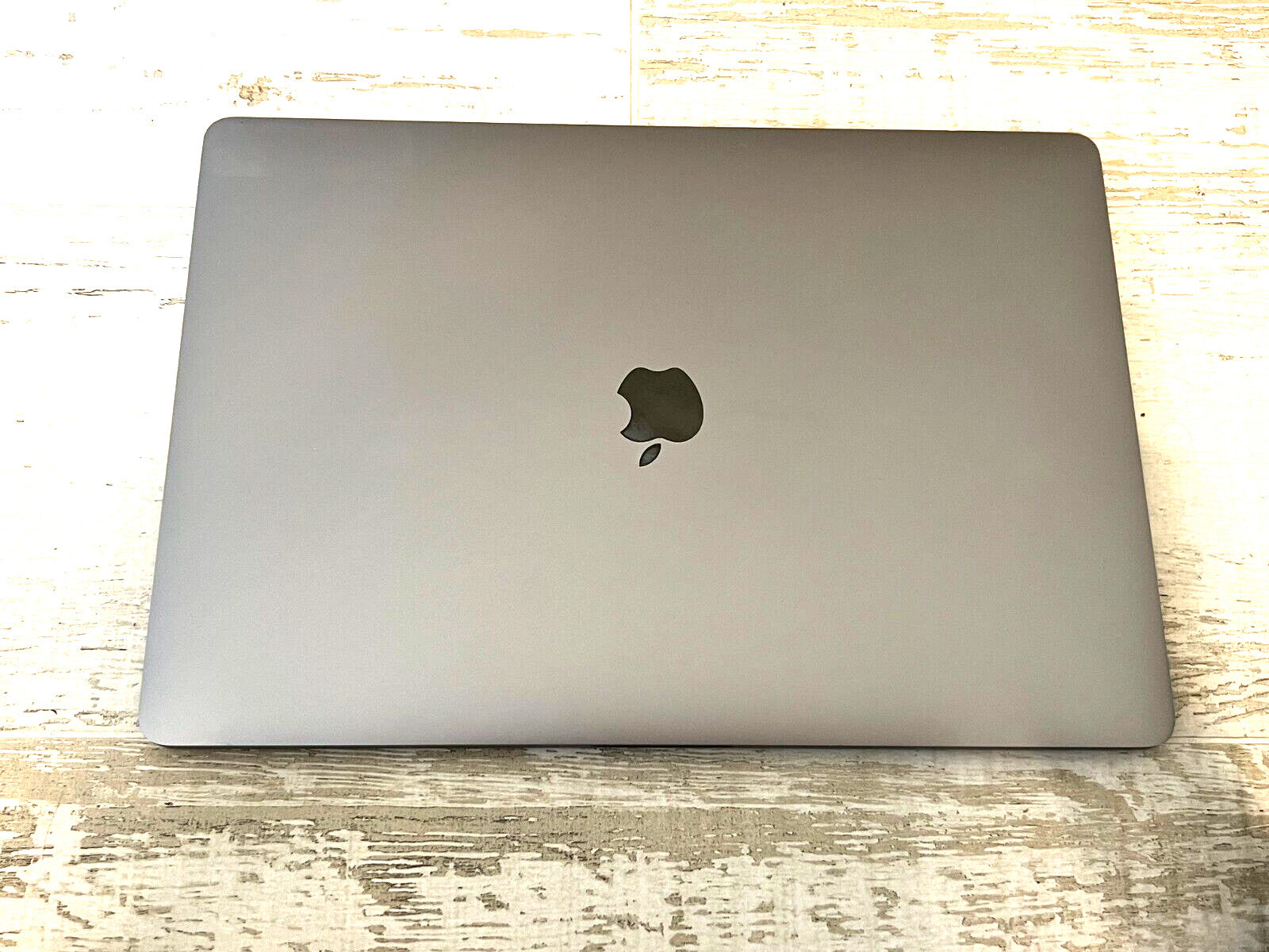 Space Gray Apple MacBook Pro 15-inch closed lid with Apple logo on rustic wooden surface, model A1990 with Touch Bar