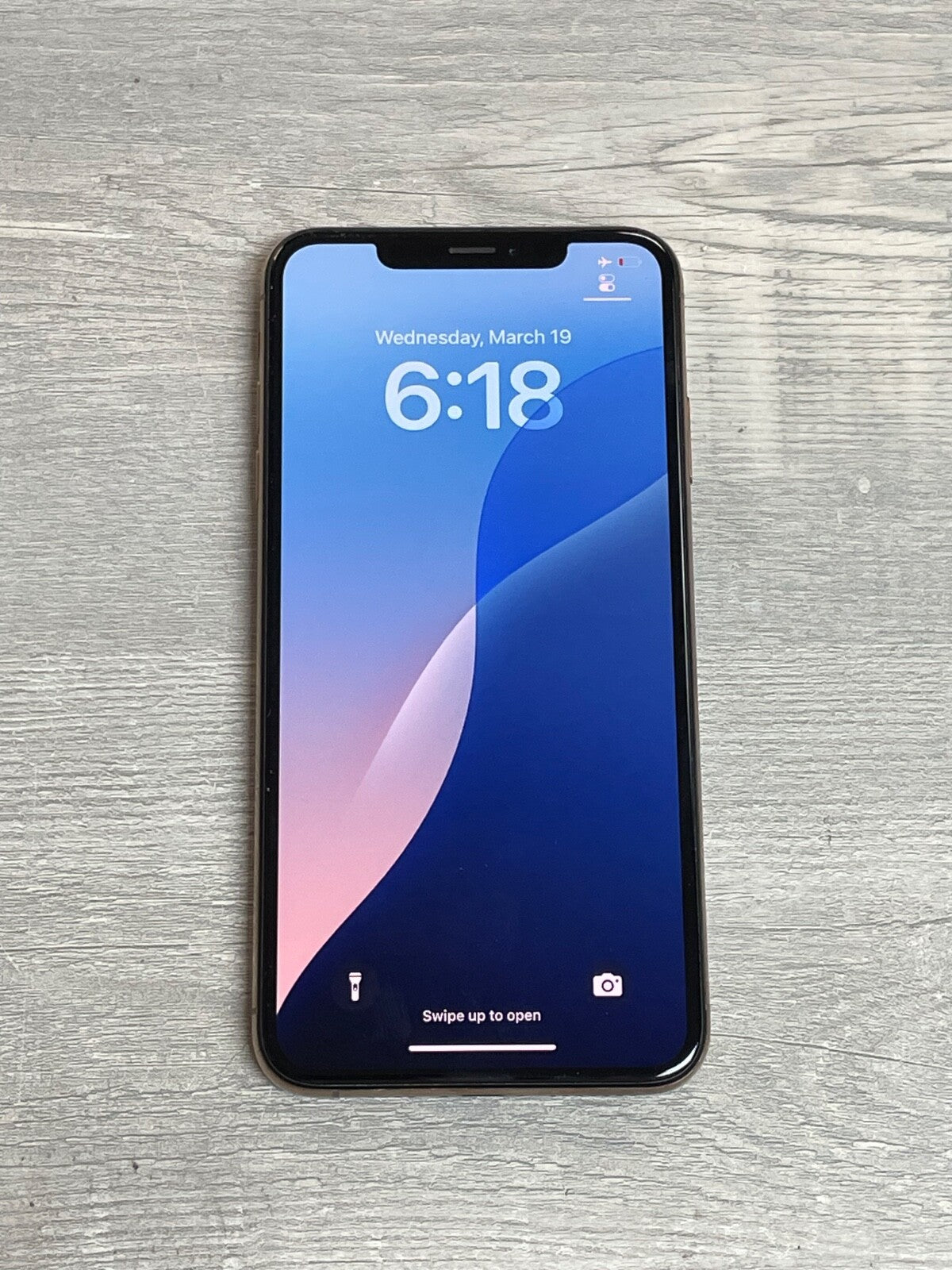 Apple iPhone XS Max displaying lock screen with time and date on wooden surface in natural light