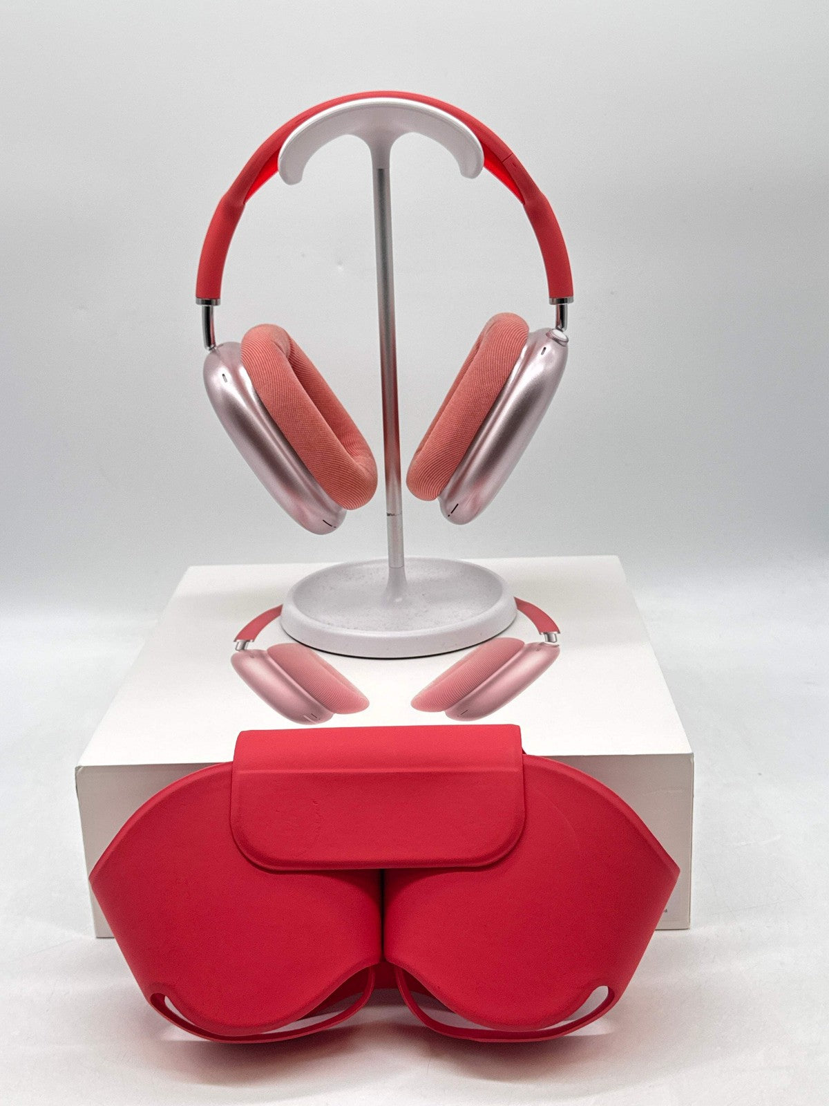 Apple AirPods Max Lightning model A2096 over-ear headphones in pink with cushioned ear cups and matching red carrying case displayed.