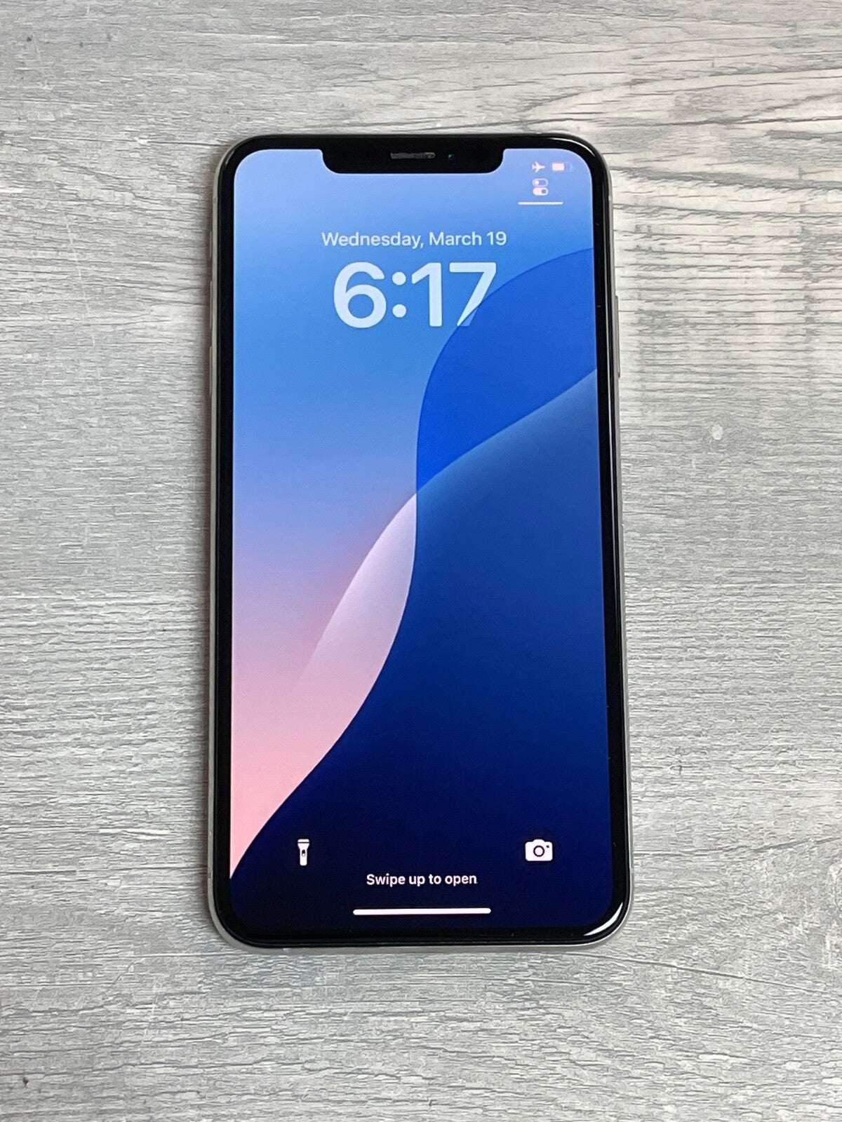 Apple iPhone XS Max displaying lock screen with time and date on a wooden surface background