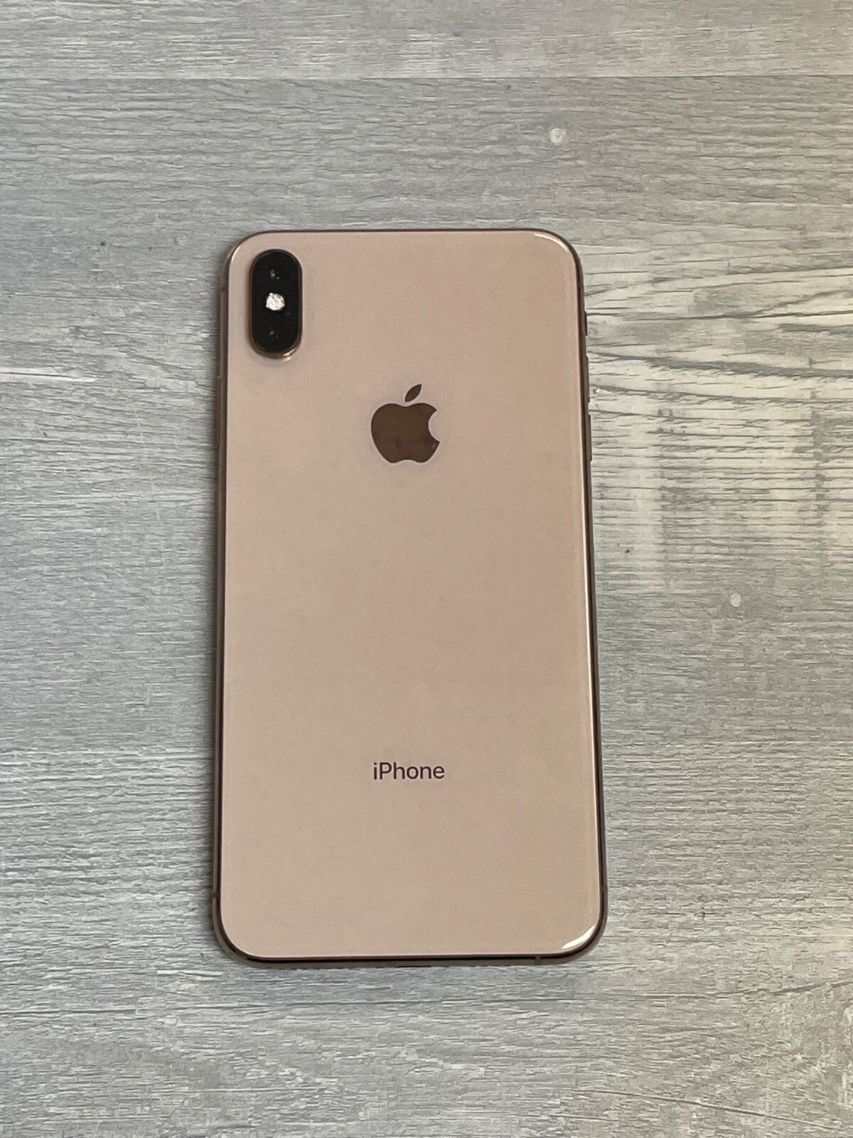 Apple iPhone XS Max in gold color showing the back with dual camera and Apple logo on wooden surface