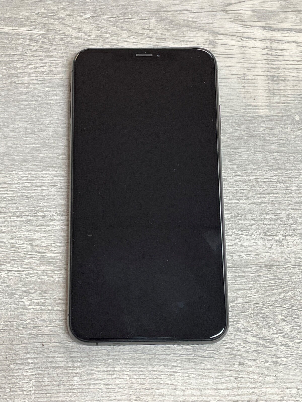 Apple iPhone XS Max with 6.5-inch screen and black front display lying on a wooden surface.