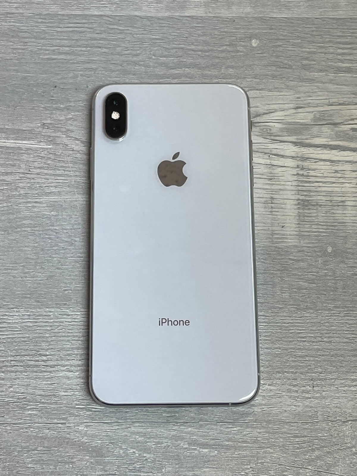 Apple iPhone XS Max in silver showing back with dual camera and Apple logo on wooden surface background