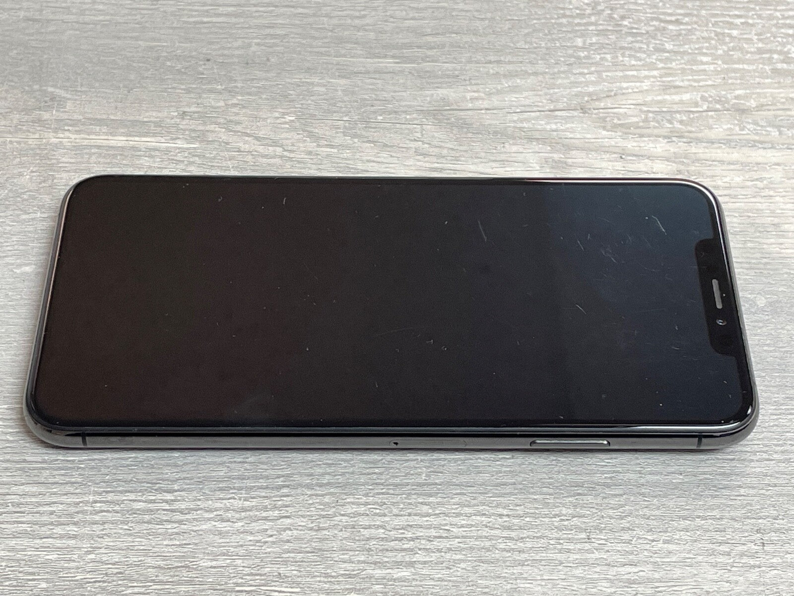 Apple iPhone XS Max with 6.5-inch screen lying face up on a light wooden surface, unlocked and in black color.