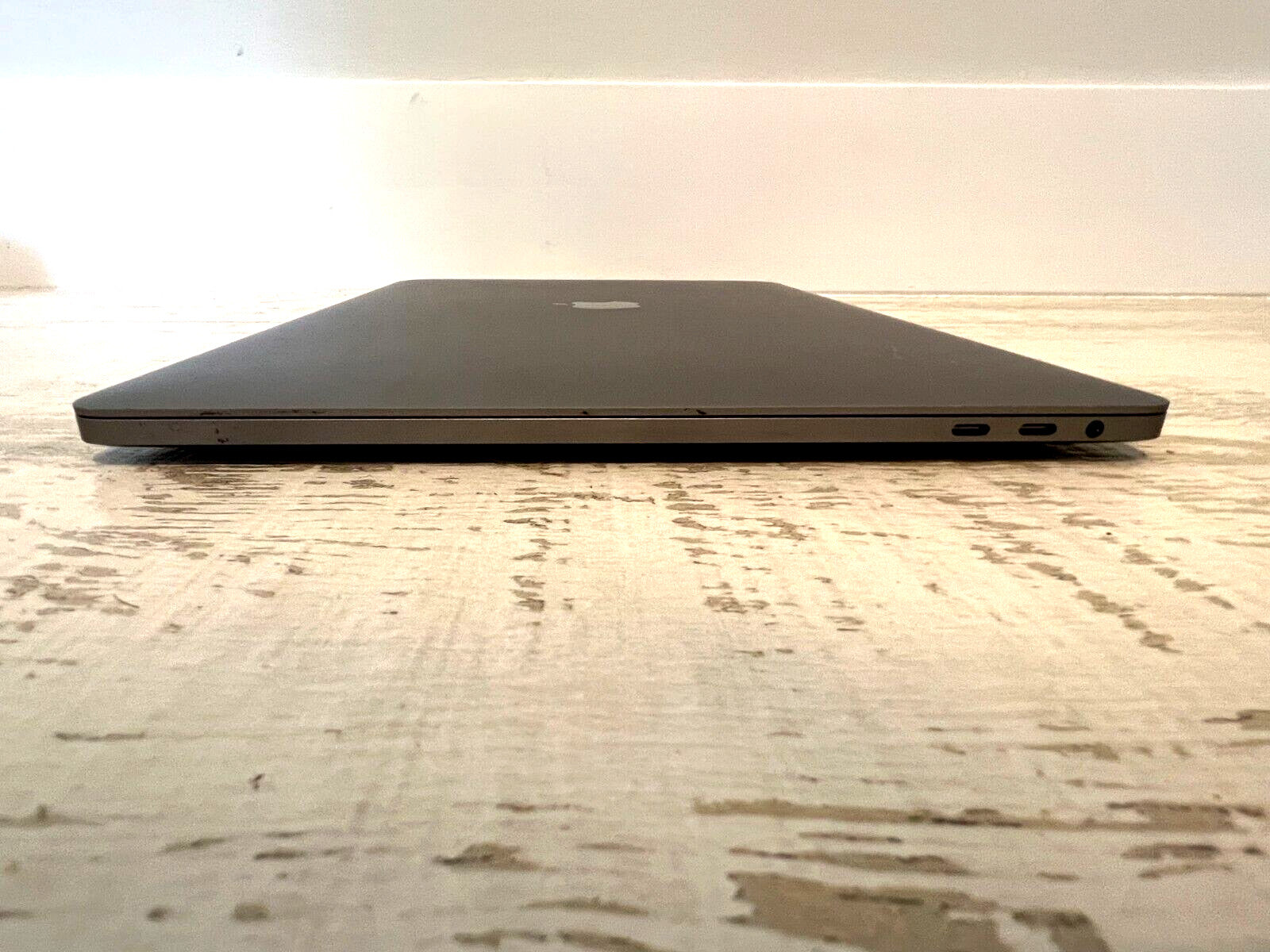 Space Gray Apple MacBook Pro 15-inch closed view showing slim profile with Thunderbolt and headphone ports, sequoia warranty included