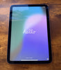 Apple iPad Mini 6th Gen purple tablet showing front screen with hello welcome message on wooden surface background