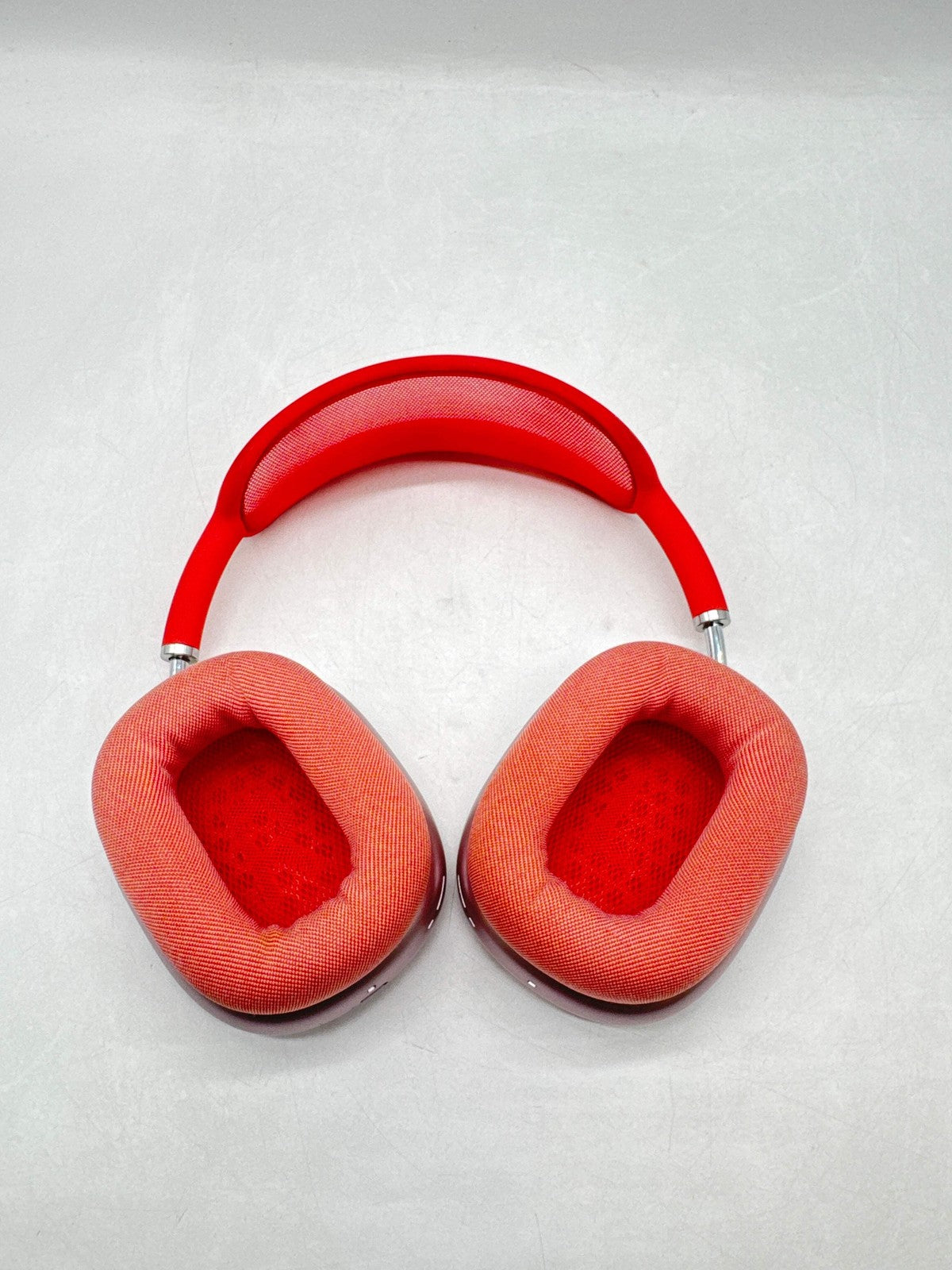Red Apple AirPods Max over-ear headphones with breathable mesh ear cushions and adjustable headband shown flat on surface
