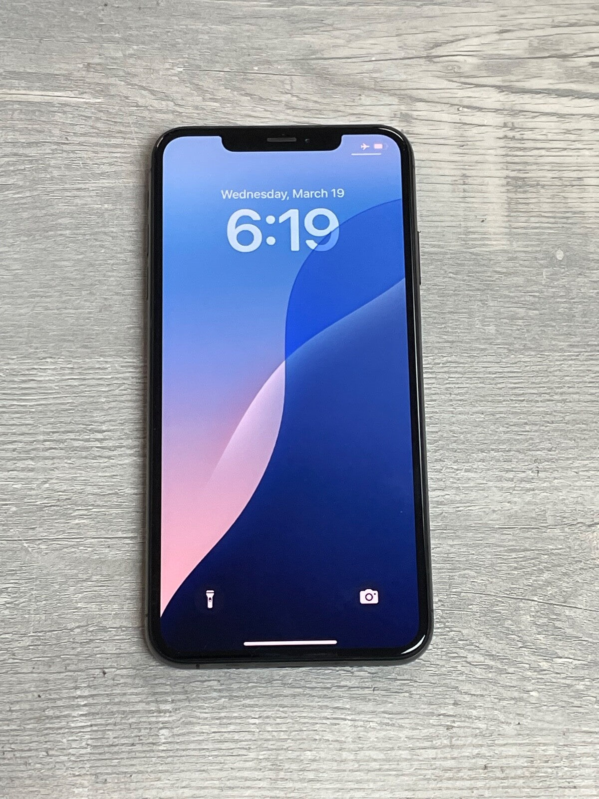 Apple iPhone XS Max with 6.5-inch screen displaying time and date on a wooden surface background.