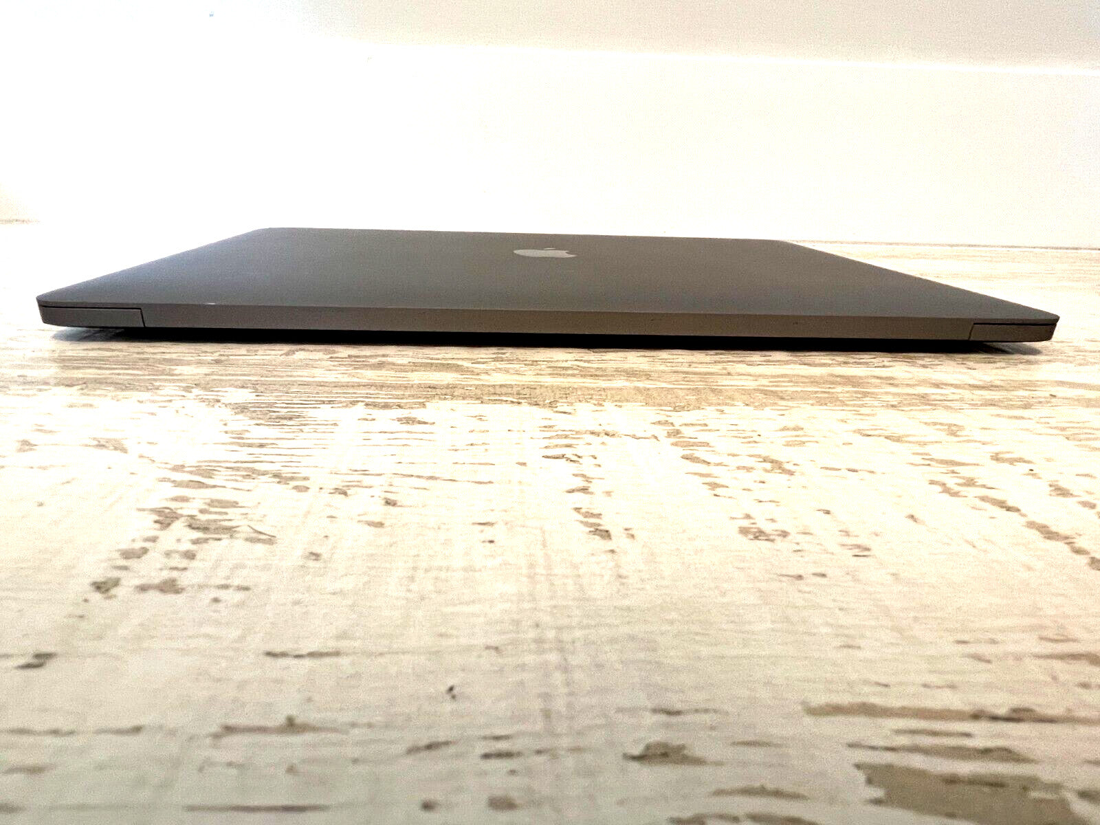 Closed Apple MacBook Pro 15-inch with Sequoia finish on textured wooden surface, Touch Bar model A1990