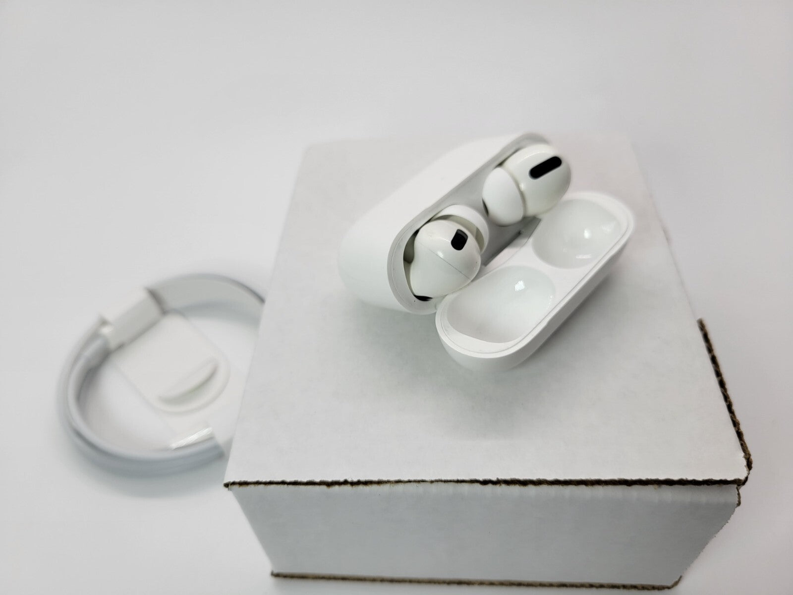 Apple AirPods Pro with wireless charging case open on white box with charging cable nearby in very good condition