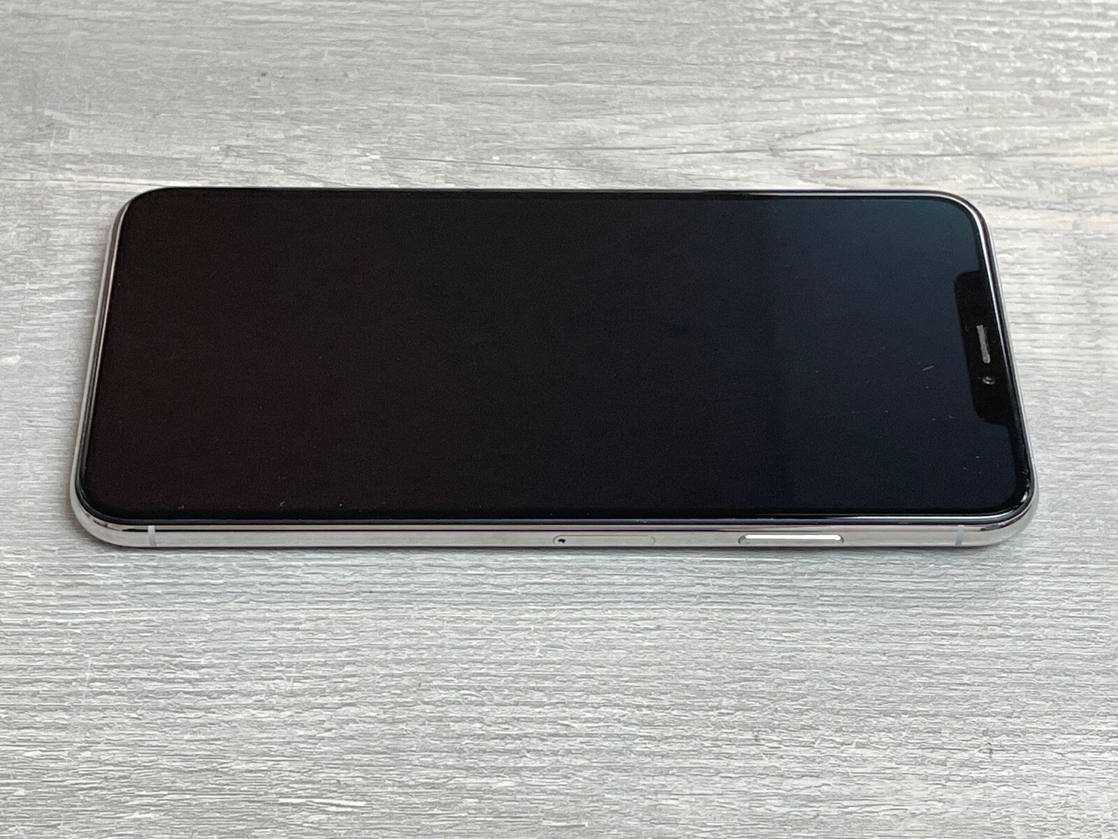 Apple iPhone XS Max lying flat with screen off showcasing sleek design and silver frame on wooden surface