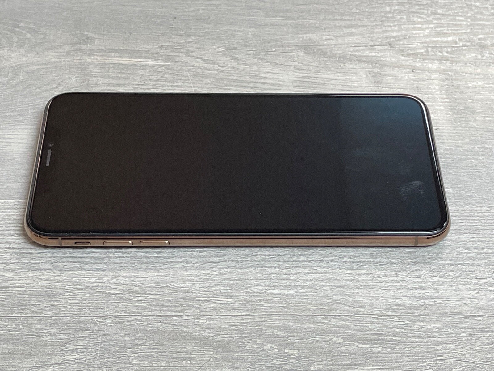Apple iPhone XS Max with 6.5-inch screen laying flat on a wooden surface showing the front display and side buttons.