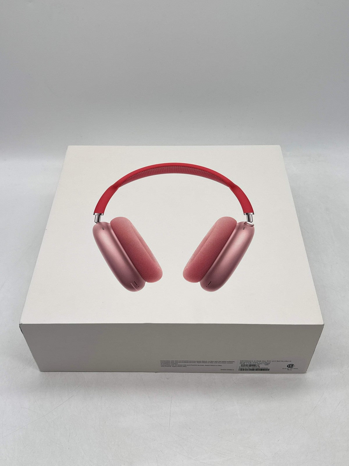 Apple AirPods Max pink over-ear headphones displayed on white retail box with red headband and cushioned ear cups