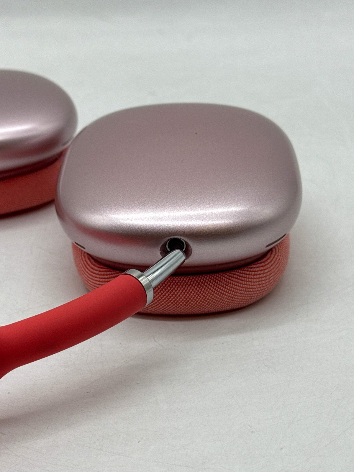 Close-up of Apple AirPods Max A2096 pink ear cup with red headband, showing seamless metal frame and mesh fabric cushion