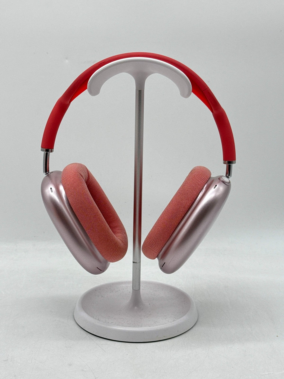 Apple AirPods Max Lightning A2096 over-ear headphones in pink with red headband, shown on white stand front view